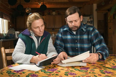 Woman seated at table writes in checkbook while man next to her holds document_GettyImages-86529035