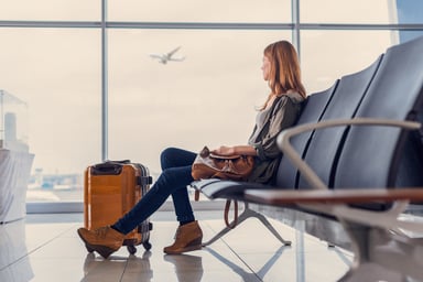 Woman seated in airport watching plane through window_GettyImages-627281458