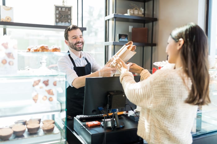 Smiling man handing bag of bread to woman