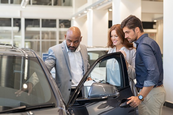 A salesman shows a couple the interior of a car.