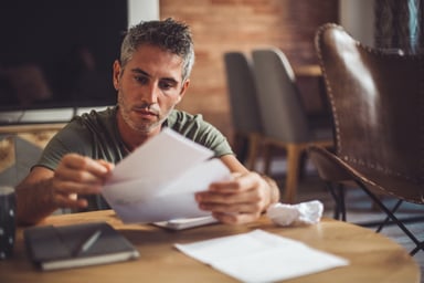 Man at table with serious expression holding envelope_GettyImages-1163762156