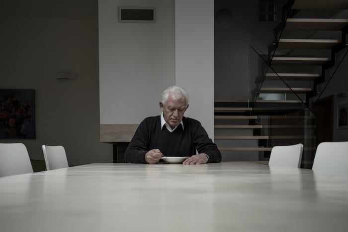 Sad old man eating alone in house.