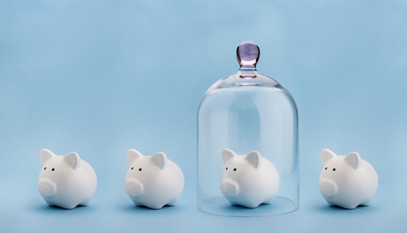 three piggy banks with one covered by a clear upside-down glass jar protecting it.