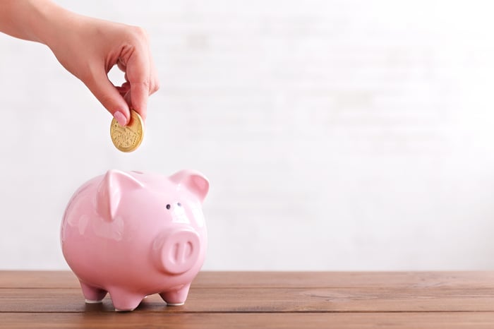 Hand putting coin in pink piggy bank.