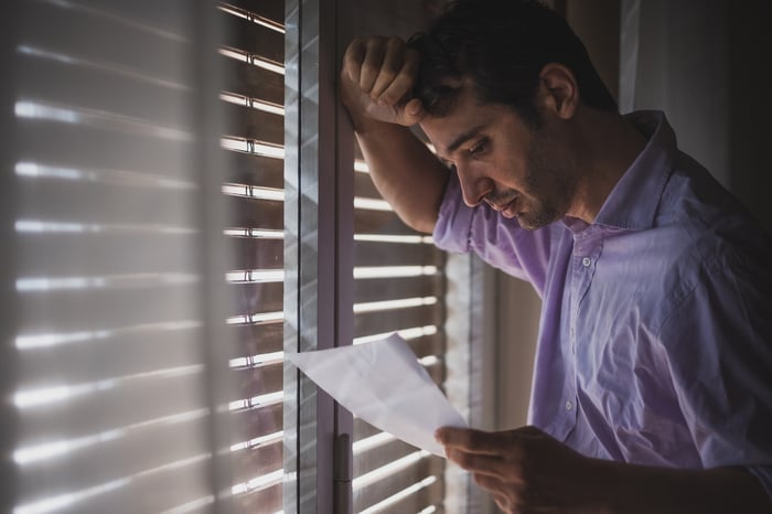 Man resting head against window, holding document