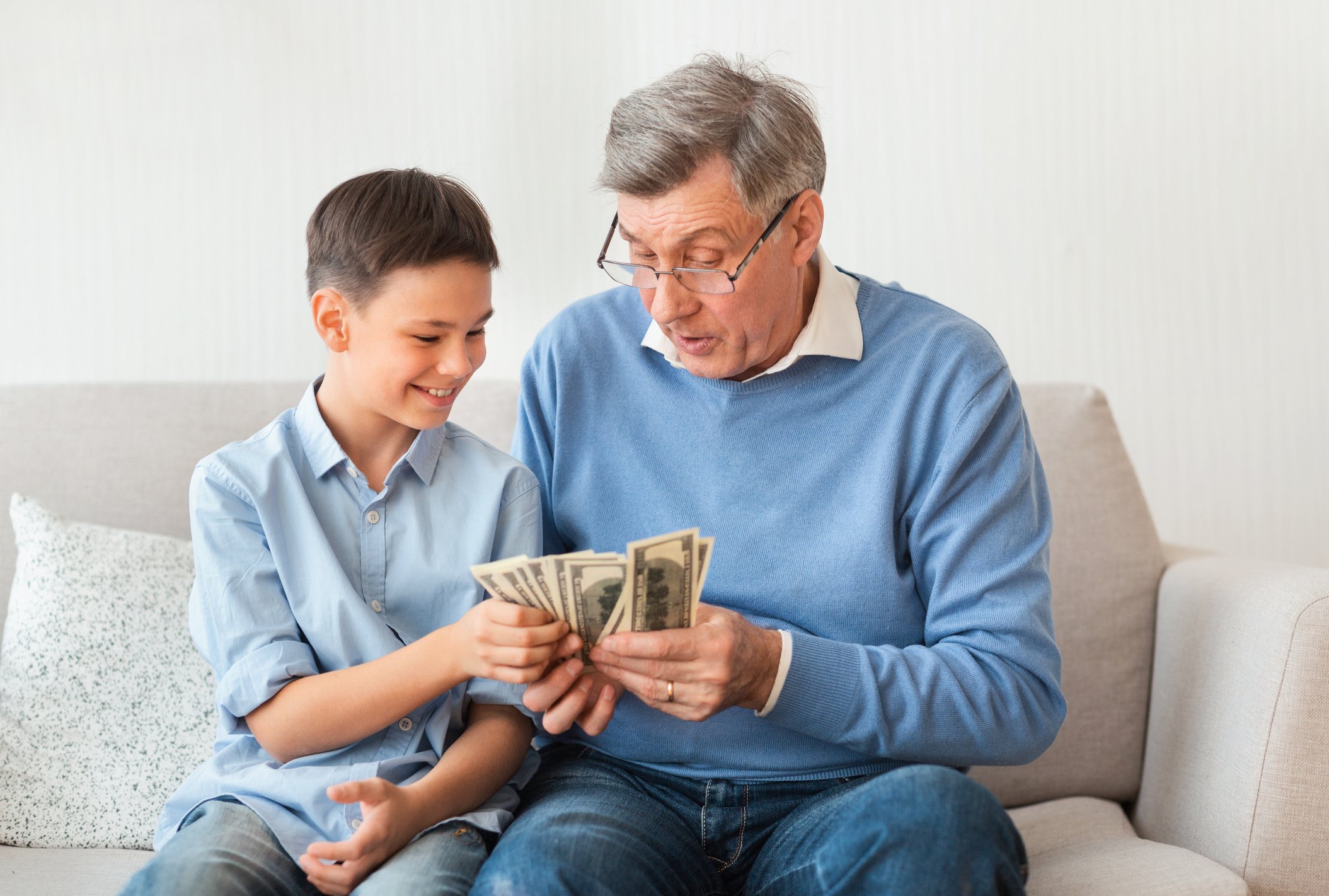 Grandad sitting on a couch counting through a wad of money with his grandson
