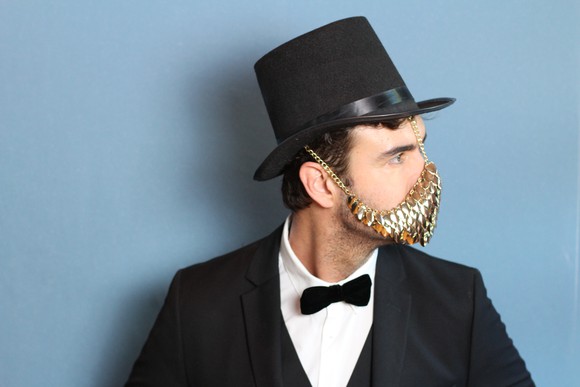Man in tuxedo and top hat wearing a golden face mask.