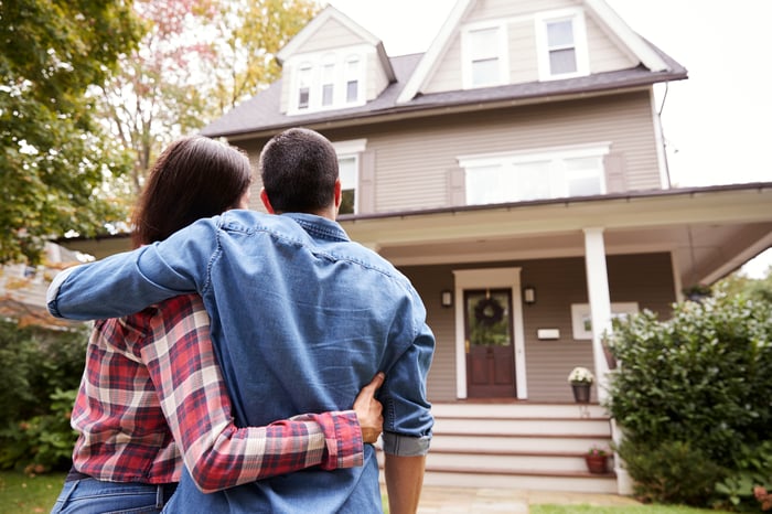 A couple embraces in the front yard in front of their new home.