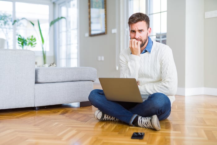 Man sitting on floor with laptop in lap biting nails