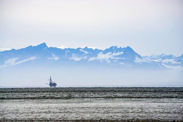 An oil platform in the icy waters off Alaska with snow-capped mountains in the background.