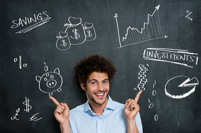 A young man is smiling in front of a blackboard with financial images on it.