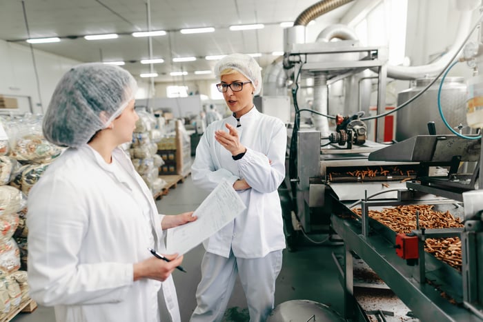 Two women in white outfits and hair coverings in bakery