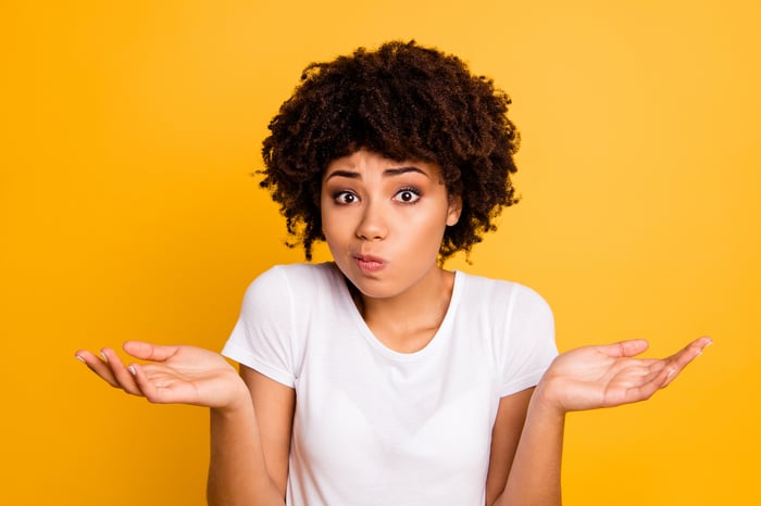 A woman shrugs in confusion against an orange background.