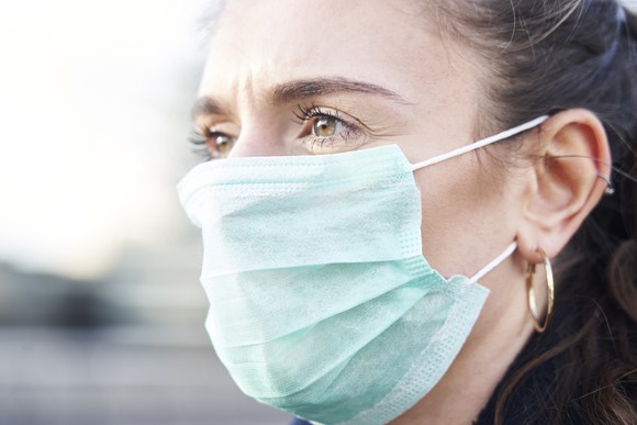 An up-close view of a woman wearing a surgical ear-loop mask.