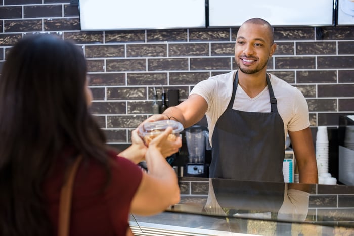Man in apron handing food carton to woman