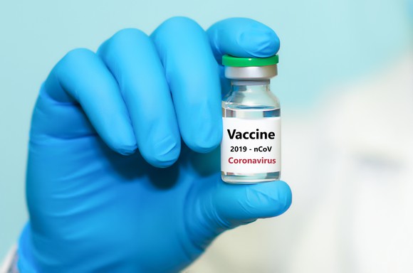 A gloved-hand holding a vial labelled "Vaccine coronavirus."