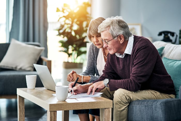 Senior couple sitting on a couch looking at a laptop
