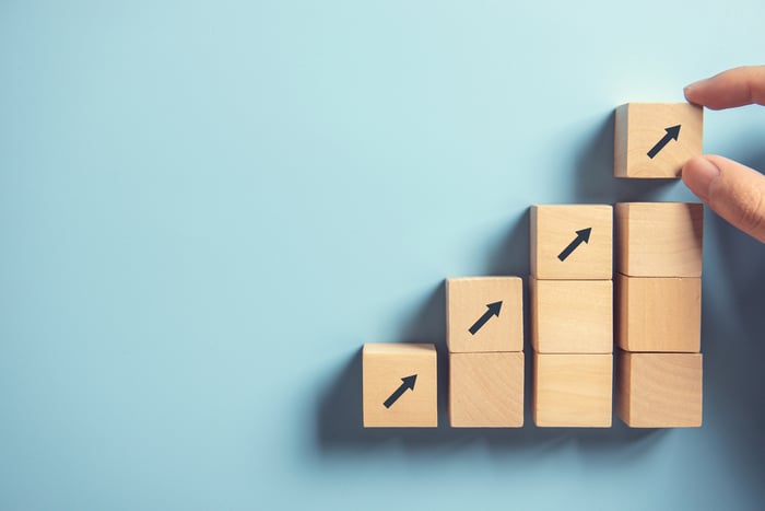 Wooden blocks are stacked in incrementally taller columns, each topped with an upward arrow block.