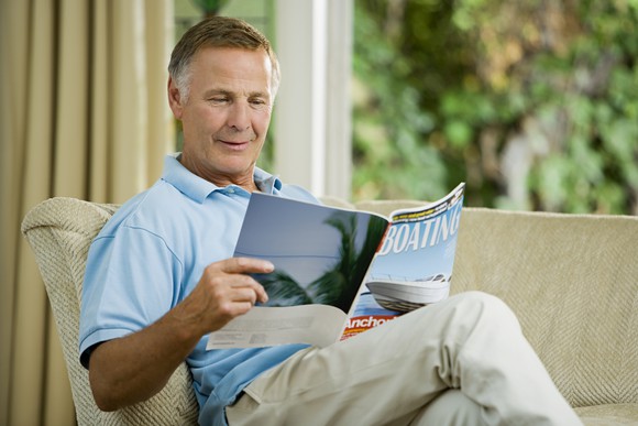 Older man sitting on couch reading  magazine