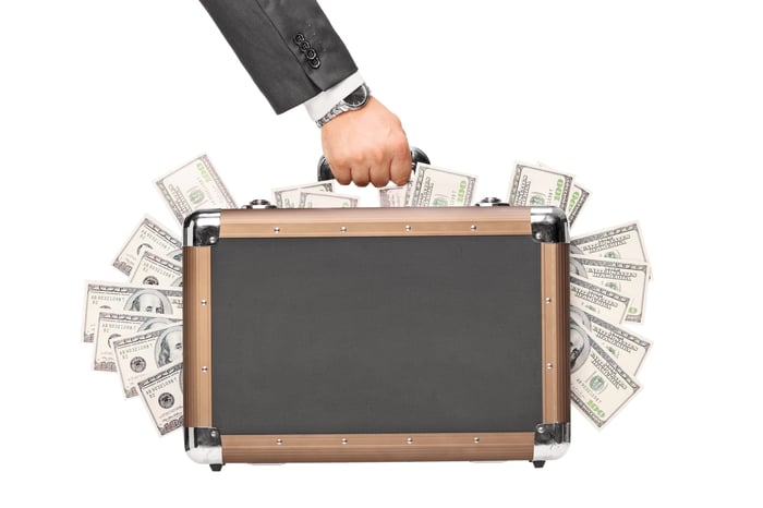 Hand holding briefcase with $100 bills sticking out