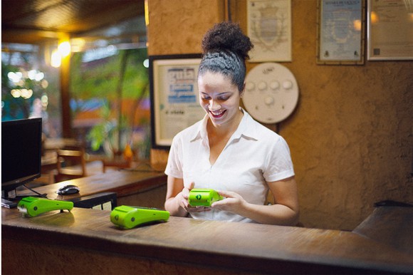 A woman in a store using a green StoneCo point of sale device.
