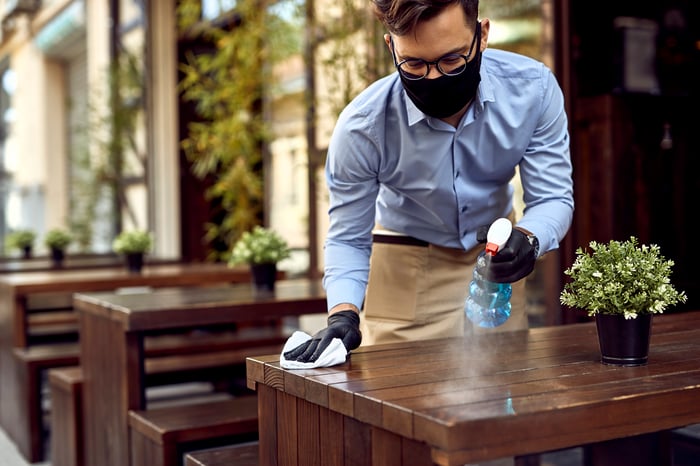 Man in mask and gloves sprays down table