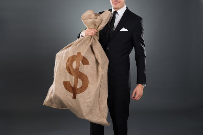 Man in a business suit carrying a large burlap sack with a dollar sign.