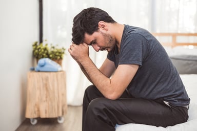 Seated man with sad expression resting head against his hands_GettyImages-1154062785