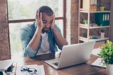 Man at laptop holding his face and grimacing_GettyImages-929128392