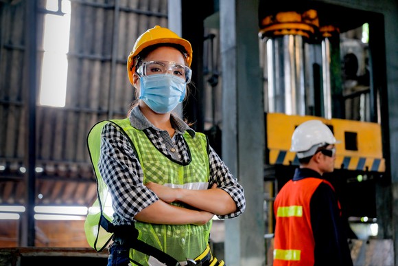 Factory worker with hygienic mask stand with confident action with her co-worker in the background.