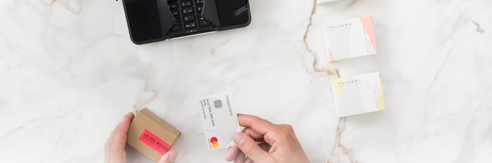 Overhead shot of a person about to feed a Mastercard into a card reader.