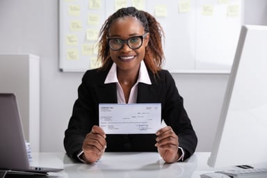 Smiling professionally dressed woman holding paycheck_GettyImages-1150345121