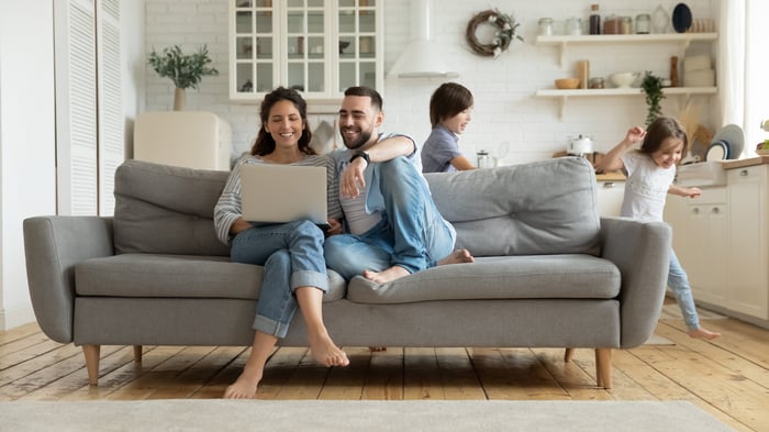 Man and woman on couch with laptop with kids running around room