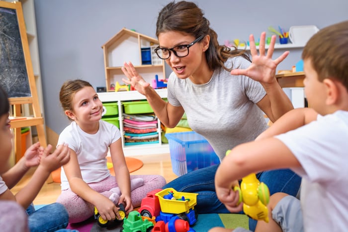 Woman seated on floor gesturing toward young children seated near her