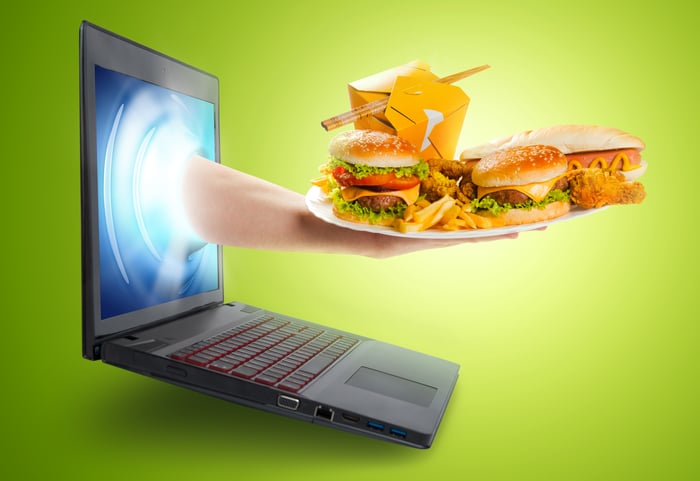 A hand emerges from laptop bearing a platter of food.