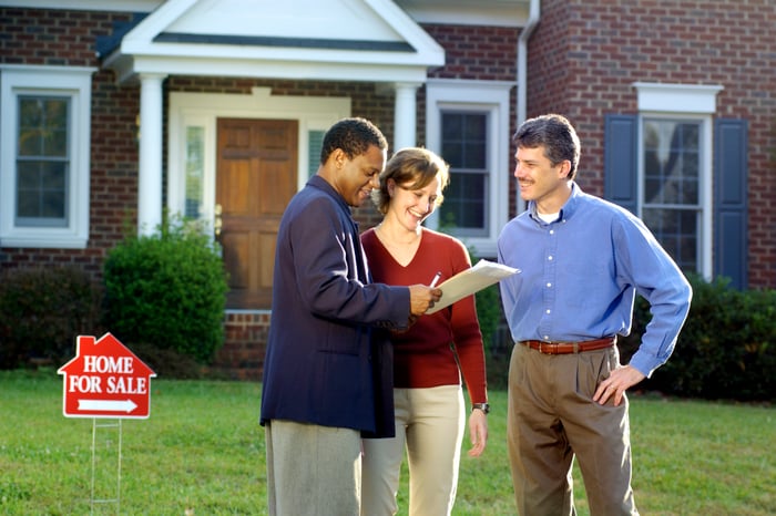 Three people in front of a house with a for sale sign on the lawn