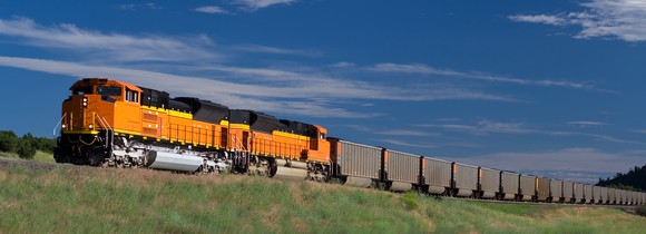 A yellow freight train ascends a hill under blue skies in Colorado.