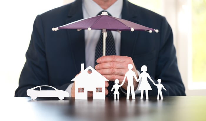 A man holding an umbrella protecting a car, house, and family