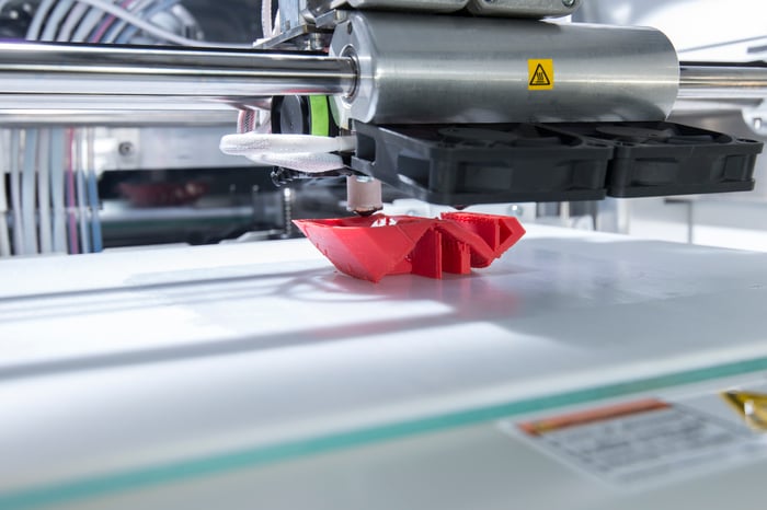 A big industrial 3D printer printing a red plastic object.