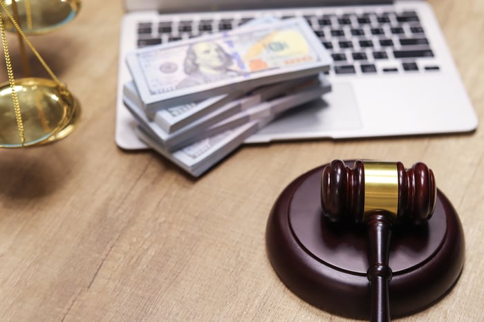 A gavel near a laptop with wrapped stacks of $100 bills on the keyboard next to a scale.