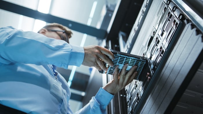 An engineer placing a hard drive into a server tower inside a data center.