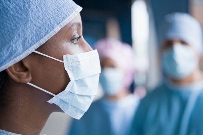 A woman in a surgical mask and attire with similarly clad people behind her