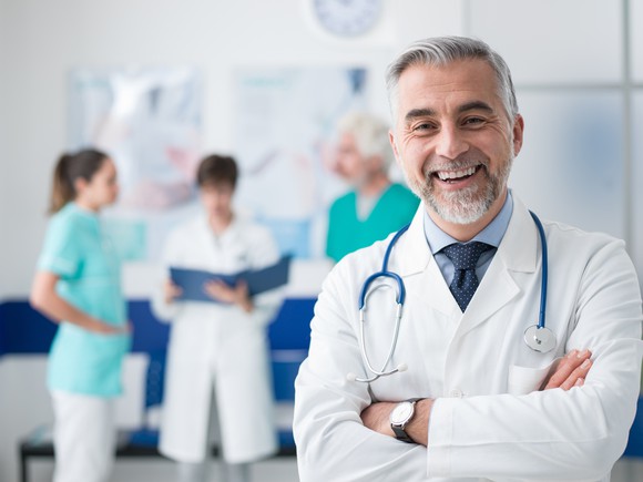 Male healthcare provider standing with arms crossed while smiling.