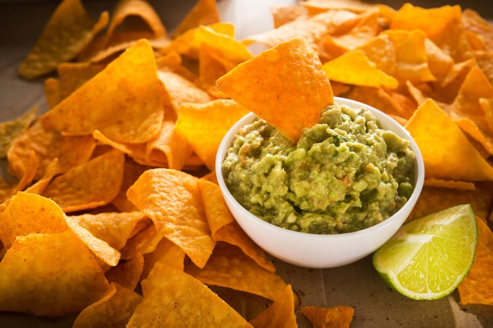 Corn chips scattered around a bowl of guacamole