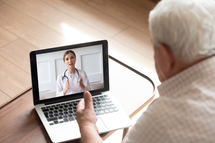 An older man talking videoconferencing with a doctor via a laptop