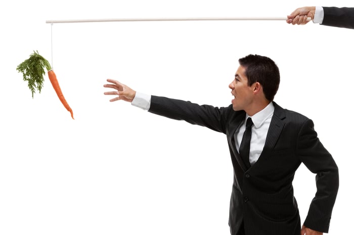 A businessman reaches for a carrot dangling from a string.