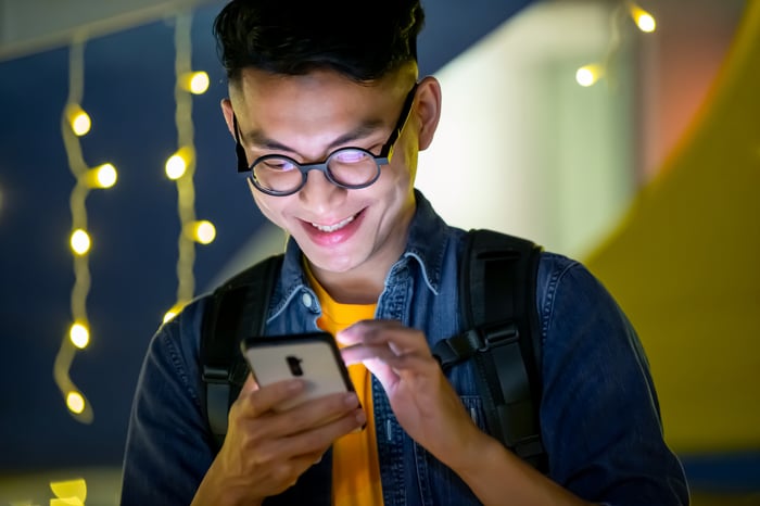 Smiling young man with face lit up by smartphone.