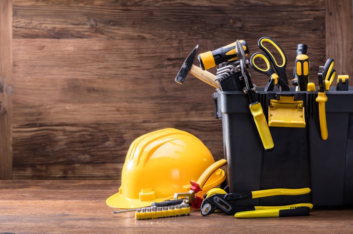 A tool box with yellow and black tools and a yellow hard hat on the floor next to it.