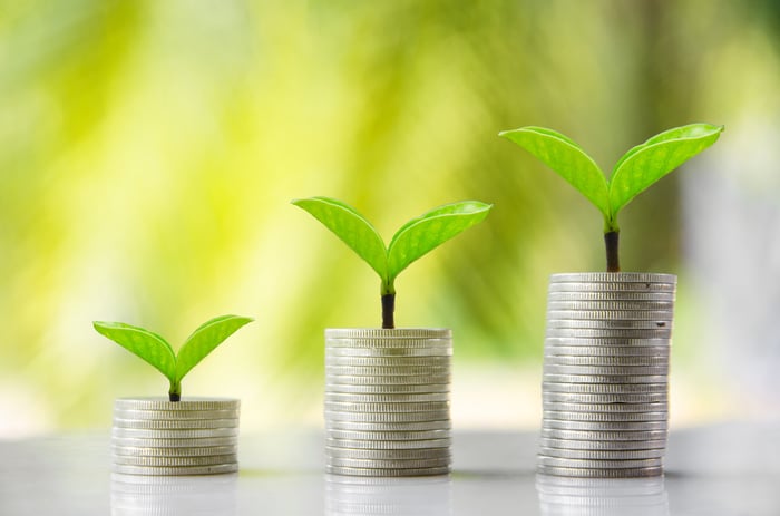 3 increasingly tall piles of coins with green leaves sprouting from them