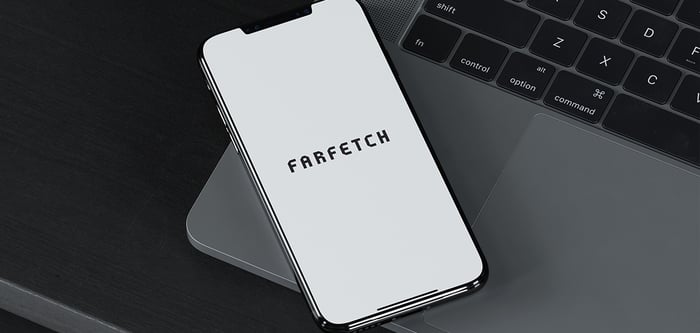 An iPhone with the Farfetch app open, resting on a laptop computer. 